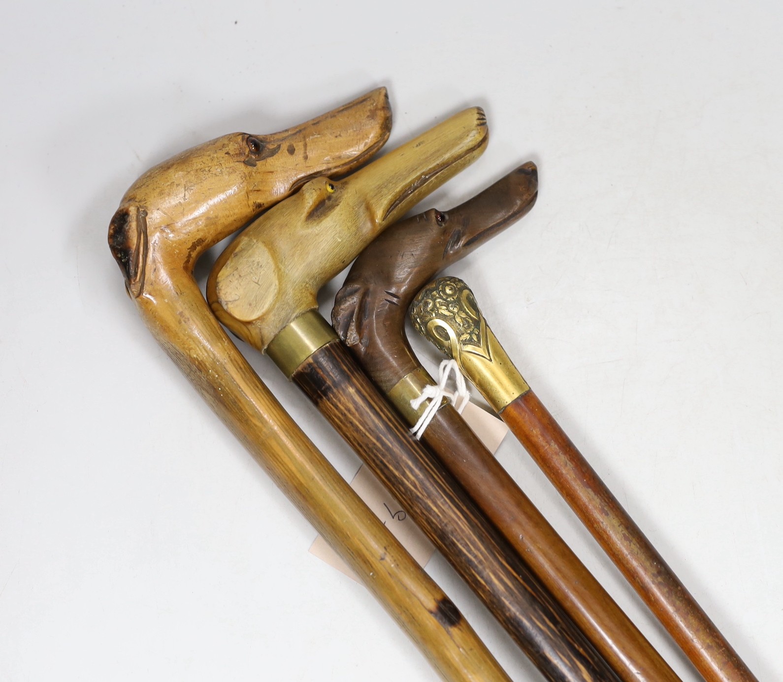 Four walking sticks: The first with carved horn dog‘s head handle, two with carved wood dogs head handles, one gilt metal mounted handle, tallest 86cms